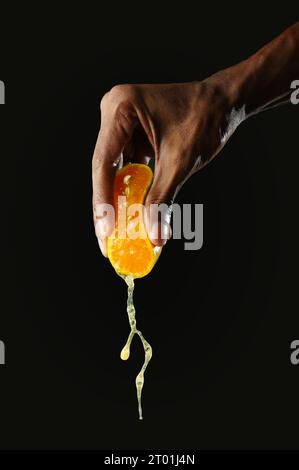 Mann hält einen Teil Orange und drückt ihn zusammen, schwarzer Hintergrund, scharfes Bild Stockfoto