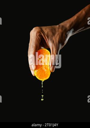 Mann hält einen Teil Orange und drückt ihn zusammen, schwarzer Hintergrund, scharfes Bild Stockfoto