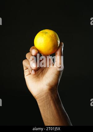 Mann hält einen Teil Orange und drückt ihn zusammen, schwarzer Hintergrund, scharfes Bild Stockfoto