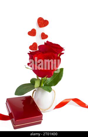 Rote Rosen in einer kleinen weißen Vase mit einer Schmuckschatulle, auf weißem Hintergrund, vertikale Fotografie Stockfoto