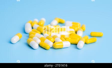 Stapel weißer und gelber Pillen auf blauem Hintergrund. Konzept der medizinischen Behandlung mit Medizin, Vitaminen oder Ergänzungsmitteln in Kapseln, Drogensucht Stockfoto