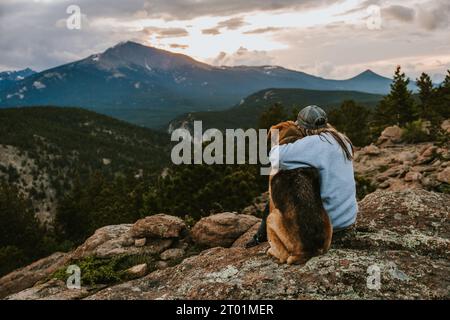 Eine Frau mit ihrem Hund, die bei Sonnenuntergang in Colorado über die Berge schaut. Stockfoto