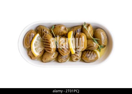 Gegrillte grüne Oliven auf einer weißen Porzellanplatte auf weißem Hintergrund Stockfoto