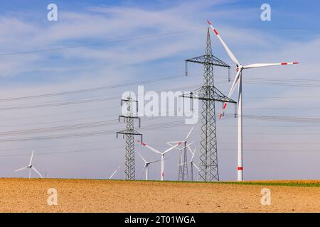 Feld mit vielen Windturbinen einer Windturbine und Stromleitungen mehrerer Strommasten unter blauem Himmel Stockfoto