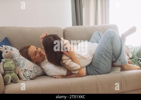 Niedliches kleines Mädchen umarmen Kuscheln aufgeregte junge Mutter zeigen Liebe und Zuneigung, lächelnde Mutter und lustige kleine Tochter haben Spaß zu Hause Umarmung teilen aus der Nähe Stockfoto