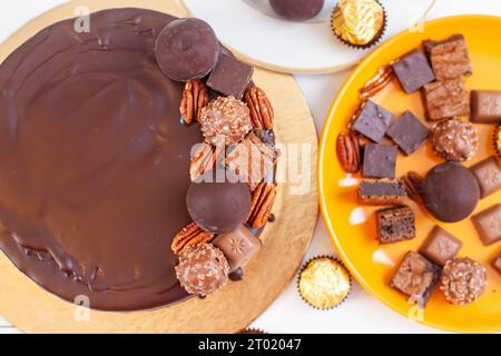 Dekoration von Schokoladenkuchen mit Schokoladenkugeln, Trüffeln, Pekannüssen, Brownie- und Toffee-Stücken, flacher Lay Stockfoto