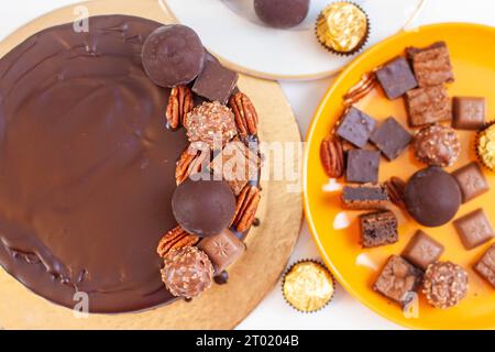 Dekoration von Schokoladenkuchen mit Schokoladenkugeln, Trüffeln, Pekannüssen, Brownie- und Toffee-Stücken, flacher Lay Stockfoto