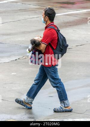 SAMUT PRAKAN, THAILAND, 06. Juni 2023, Ein Mann trägt ein Kind auf der regnerischen Straße Stockfoto