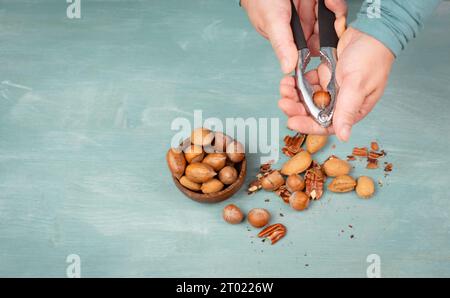 Nüsse mit einem Nussknacker knacken, verschiedene Mandeln, Haselnüsse und Pekannüsse mischen, gesunde Ernährung und Lebensstil Stockfoto