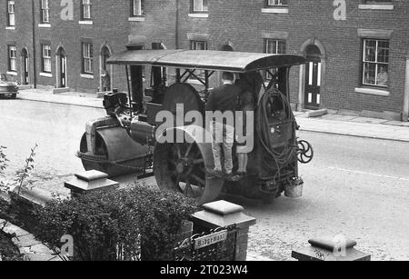 1960er Jahre, historisch, ein Mann und sein Sohn, der auf einer Metallplattform des Führerstands eines dreirädrigen Dampftraktors stand, auf dem er eine Fahrt entlang einer Straße viktorianischer Reihenhäuser in Oldham England, Großbritannien, unternahm. Stockfoto