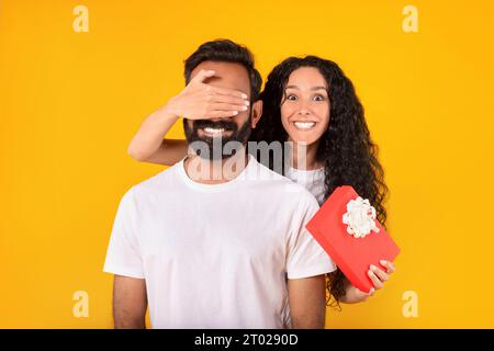 Frau aus dem Mittleren Osten schließt die Augen des Mannes und hält es mit gelbem Hintergrund Stockfoto