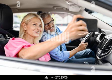 Glückliche ältere Paare fahren mit dem Auto und machen Selfie am Telefon Stockfoto