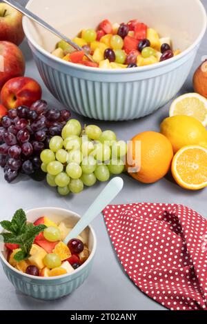 Frisch zubereiteter Obstsalat in einer großen Schüssel und passender gefüllter Dessertschüssel. Mit Obst und Minze dekoriert. Stockfoto