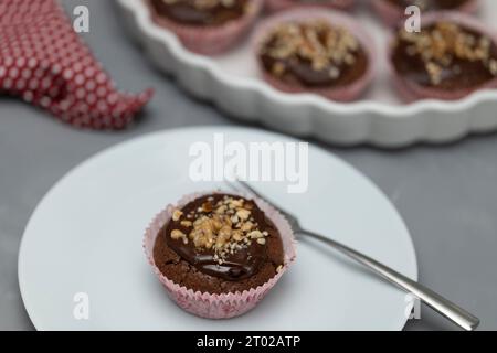 Schokoladen-Walnussmuffins serviert auf Teller. Mit Kuchenplatte und mehr Muffins im Hintergrund Stockfoto