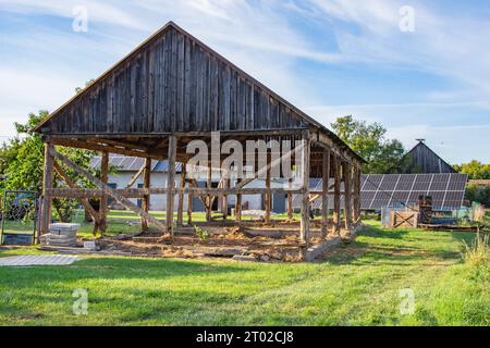 Das Skelett einer alten, zerstörten Scheune, die an einem sonnigen Tag abgerissen wird. Gras Stockfoto