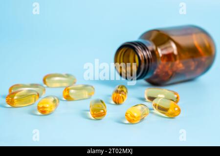 Omega-3-Kapseln in der Nähe der geöffneten Flasche auf blauem Hintergrund. Fischöl-Vitamine und Nahrungsergänzungsmittel in der Therapie oder wissenschaftlichen Forschung. Nahaufnahme, selektiver Fokus Stockfoto