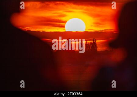 Wunderschöner wolkig-roter Sonnenuntergang mit gigantischer Sonne über großen Feldern und Bäumen, gesehen von einem 600-mm-Kameraobjektiv Stockfoto