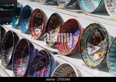 Reihen von wunderschönen, mehrfarbigen dekorativen Schalen mit verschiedenen Designs von sich wiederholenden und floralen Mustern, die auf weißen Regalen von der Seite aus gesehen ausgestellt sind Stockfoto