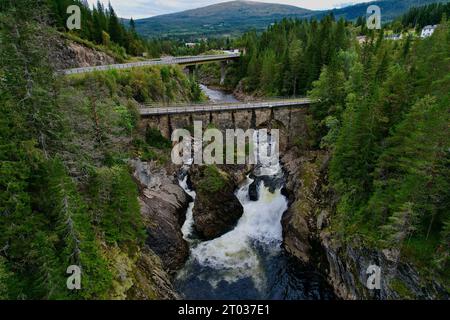 Genießen Sie die Schönheit der Natur im Herzen Norwegens: Ein ruhiger Fluss schlängelt sich durch einen Canyon, umgeben von üppigen Bäumen, während zwei Brücken die Welt verbinden Stockfoto