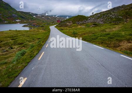 Die norwegische Panoramastraße Gaularfjellet zwischen Moskog und Balestrand an einem stürmischen Tag. Ein rotes Bauernhaus blickt um die Kurve entlang des Horizonts. Stockfoto