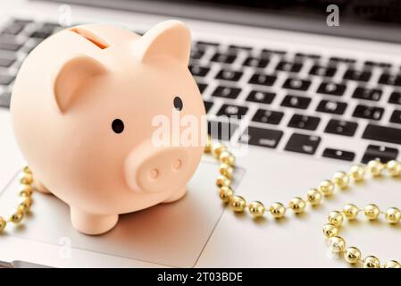 Schweinebank auf einem Laptop mit goldenem Weihnachtskordel. Konzepte: Sparen beim Online-Shopping im Urlaub. Helle Komposition mit Kopierraum. Stockfoto