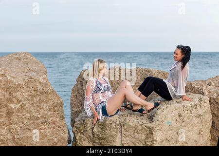 Zwei junge Mädchen sitzen und reden auf einem Felsen am Ufer des Lake Michigan Stockfoto