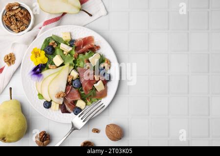 Leckerer Salat mit Brie-Käse, Schinken, Walnüssen und Birne, serviert auf weiß gekachelten Tischen, flacher Lay. Leerzeichen für Text Stockfoto