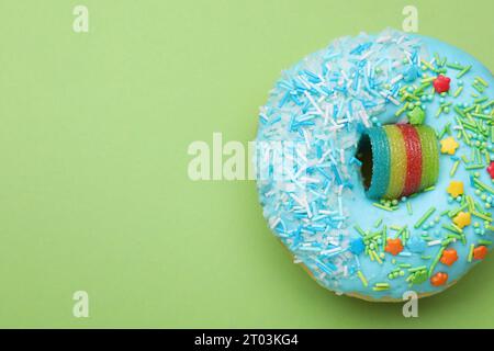 Glasierter Donut, dekoriert mit Streuseln auf grünem Hintergrund, Blick von oben. Leerzeichen für Text. Leckere Süßwaren Stockfoto