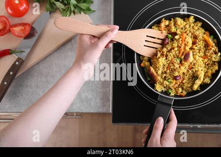 Frau frittiert Reis mit Fleisch und Gemüse auf Induktionskochfeld in der Küche, Nahaufnahme Stockfoto