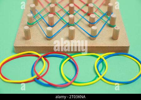 Geobord aus Holz mit Gummibändern auf grünem Hintergrund, Nahaufnahme. Lernspielzeug für die Entwicklung motorischer Fähigkeiten Stockfoto
