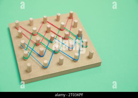 Hölzerne Geoboard mit Gummibändern auf grünem Hintergrund. Lernspielzeug für die motorische Entwicklung Stockfoto