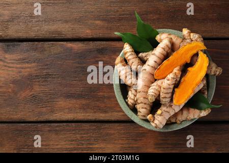 Schüssel mit frischen Kurkuma-Wurzeln und Blättern auf Holztisch, Draufsicht. Leerzeichen für Text Stockfoto