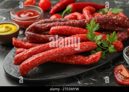 Dünne, trocken geräucherte Würstchen, serviert auf schwarzem Marmortisch, Nahaufnahme Stockfoto