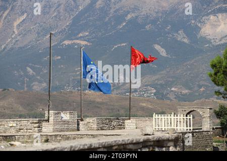 Eine blaue Flagge mit gelben Sternen und einem albanischen schwarzen Doppeladler auf rotem Hintergrund Besa, Fluss in der Brise mit Bergkulisse am Gjirokaster Castle Stockfoto