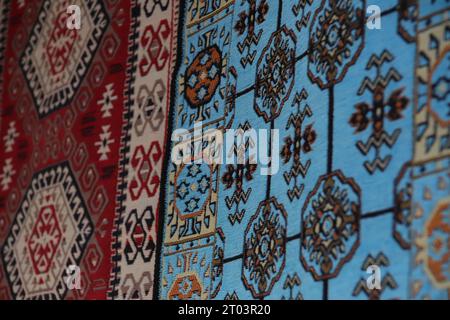 Zwei wunderschöne, mit ethnischen Mustern versehene Teppiche, ein blauer und ein roter Teppich, hängen an einer Wand, die in den Straßen des Gjirokaster Baazar in Albanien ausgestellt wird. Stockfoto