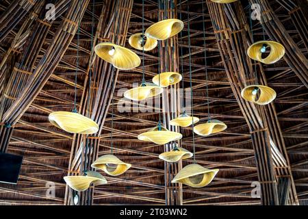 Bewundern Sie die wunderschönen handgefertigten Kronleuchter, die in einem luxuriösen Café mit einer Decke aus Bambus und Rattan hängen Stockfoto