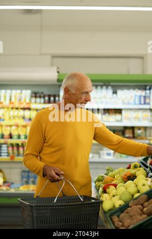 Ein älterer Mann pflückt Obst Gemüse auf der Theke im Supermarkt. Senor man, der auf dem Markt in der Nähe eines Gemüsekaufhauses mit einkauft Stockfoto