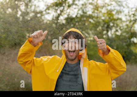 Glücklicher araber, der das Wetter im Regen in einem gelben Regenmantel im Park genießt Stockfoto