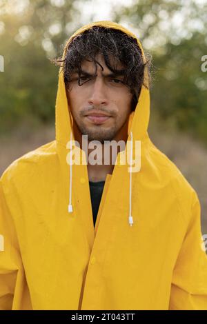 Porträt eines arabischen Mannes in einem gelben Regenmantel, der im Regen nass wird. Reisen bei schlechtem Wetter. Verärgerter junger Mann draußen Stockfoto