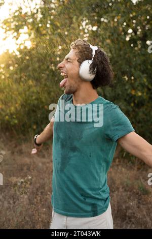 Arabischer junger Mann, der tanzt und Musik hört und den warmen Sommerregen genießt, drückt Freude aus Stockfoto