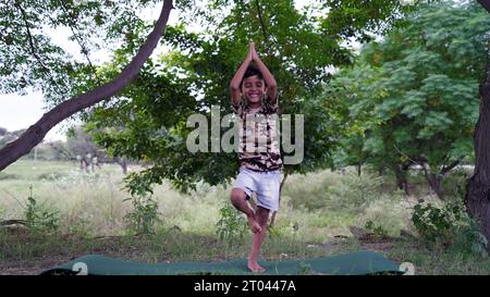 Charmanter kleiner Junge, der ernsthafte Yoga-Meditation im Garten macht. Kleiner indischer Junge, der Meditation macht Stockfoto