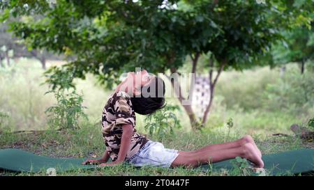 Charmanter kleiner Junge, der ernsthafte Yoga-Meditation im Garten macht. Kleiner indischer Junge, der Meditation macht Stockfoto