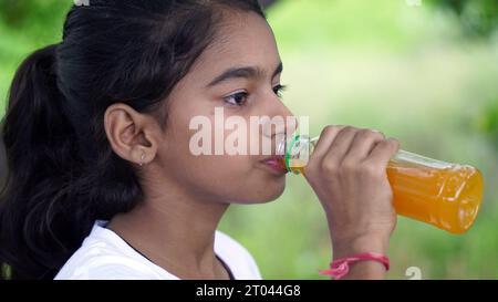 Mädchen trinkt Saft. Asiatisches Kind trinkt aus Plastikflasche. Porträt eines Mädchens, das Orangensaft trinkt. Orangensaft in der Flasche. Menschen trinken Energie dri Stockfoto