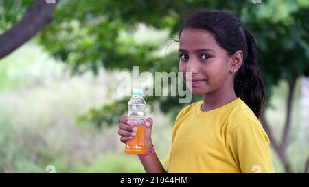 Mädchen trinkt Saft. Asiatisches Kind trinkt aus Plastikflasche. Porträt eines Mädchens, das Orangensaft trinkt. Orangensaft in der Flasche. Menschen trinken Energie dri Stockfoto