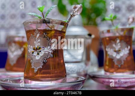 Maurischer Tee mit Minze, traditionelles marokkanisches Getränk in dekorierten Kristallgläsern, silberne Teekanne und Zuckerschale im Hintergrund Stockfoto