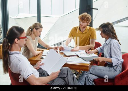 Vier junge Kollegen in smarten Outfits konzentrieren sich stark auf ihre Arbeitspapiere, das Coworking-Konzept Stockfoto