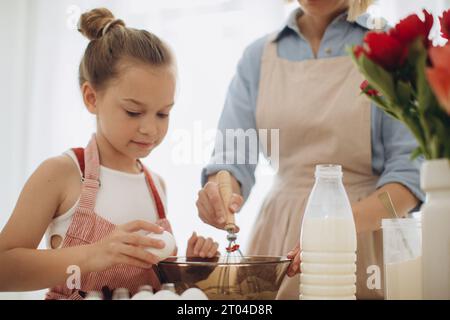 Mutter und Tochter bereiten Pfannkuchenteig vor. Eine Mutter bringt ihrer 8-jährigen Tochter das Kochen bei. Stockfoto