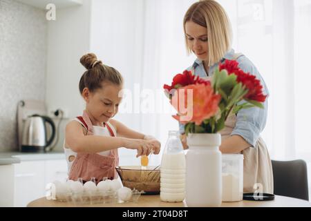 Mutter und Tochter bereiten Pfannkuchenteig vor. Eine Mutter bringt ihrer 8-jährigen Tochter das Kochen bei. Stockfoto