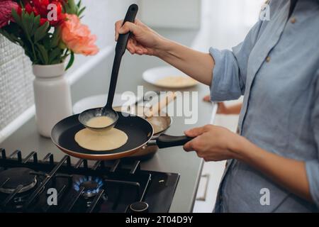 Eine junge Mutter und ihre kleine Tochter kochen zusammen Pfannkuchen zum Frühstück. Mutter bringt Tochter das Kochen bei. Stockfoto