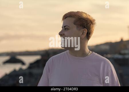 Ein strahlendes, nicht-binäres Individuum, das ein fröhliches Lächeln zeigt. Ihr kurzgefärbtes Haar unterstreicht in diesem Porträt noch mehr ihre lebendige Persönlichkeit Stockfoto